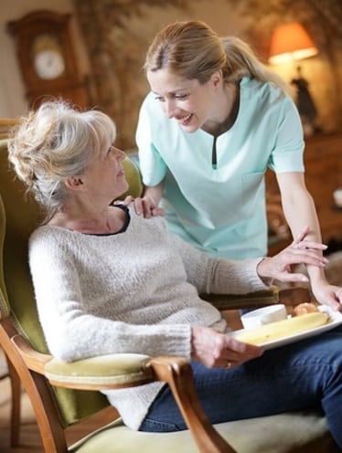 care worker supporting an elderly lady in a care home and giving her lunch
